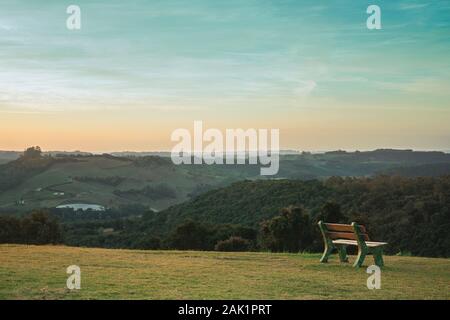 Banco solitario sul prato verde e boscosa valle, in un paesaggio bucolico al tramonto vicino a Bento Goncalves. Un paese produttore di vino città nel sud del Brasile. Foto Stock