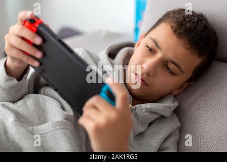 Ragazzo riproduce i video giochi su una console portatile mentre giaceva su un divano Foto Stock