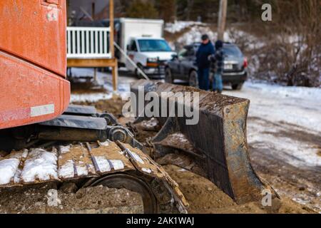 Chiudere i dettagli di una lama di riempimento, aka apripista, di un mini escavatore al lavoro su un cantiere con costruttori sfocate e site in background Foto Stock