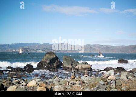 Spiaggia rocciosa con vista delle promontori di Marin attraverso la baia da Mile Rock Beach, San Francisco. Mile Rocks Faro in lontananza. Foto Stock