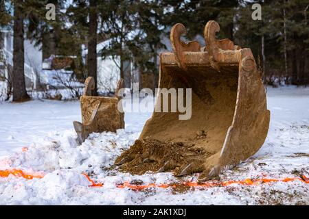 Parti di un escavatore sono visti su un cantiere in inverno. Un cucchiaio di acciaio con denti da un dipinto di linea pronto per lo scavo di fossi e basi Foto Stock