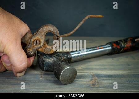 Maschio di mano che tiene il vecchio arrugginito impugnature e piegato lungo corroso chiodo su una tavola in legno rustico in una vista ravvicinata Foto Stock