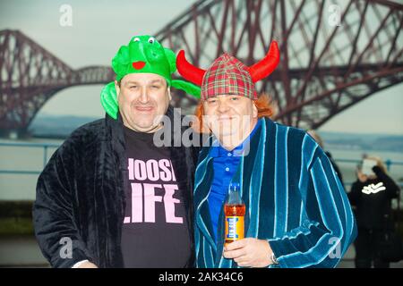 Festaioli indossando abiti fantasiosi per il tradizionale giorno di nuovi anni Loony Dook con il celeberrimo Ponte di Forth in background Foto Stock