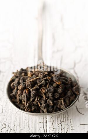 Cumulo di materie, essiccato cannella dei boccioli spice in metallo scoop su bianco rustico sfondo tabella con il fuoco selettivo Foto Stock