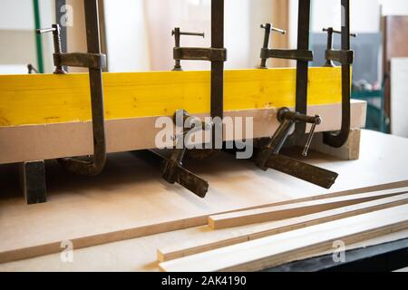 Plank e il blocco di legno in una morsa di carpentieri su un banco di lavoro in un laboratorio di falegnameria tenuto saldamente nelle pinze di bloccaggio Foto Stock