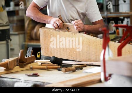 Carpenter spianare un blocco di legno con una ruspa per smussare il bordo in una officina per la lavorazione del legno in una chiusura su strumenti sul banco di lavoro con le mani e shavin Foto Stock