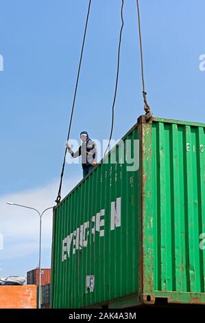 Jakarta, Indonesia - 2019.12.18: un impresa di movimentazione in piedi su una gru sollevati contenitore dopo aver collegato i cavi di sollevamento in corrispondenza di Sunda Kelapa port Foto Stock