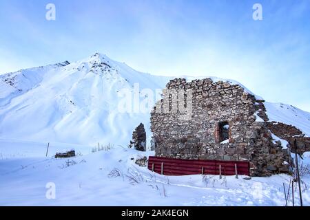 Le rovine di un antico edificio sullo sfondo di una montagna innevata a croce Pass georgiano autostrada militare durante il tramonto Foto Stock