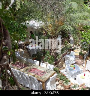 A s una cameriera tabelle prepara uno non può aiutare ma lo sguardo al bellissimo giardino circonda del ristorante Avli a Rethymnon, Creta. Foto Stock