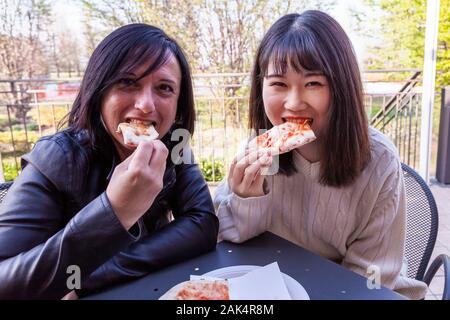 Giovani fidanzate multi-etnico femmine mangiare una gustosa pizza all'aperto Foto Stock