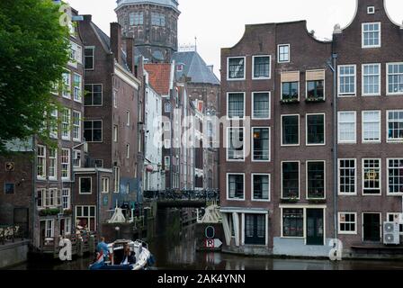 Edificio ad Amsterdam all'aperto con il fiume che passa tra gli edifici e una barca che attraversa gli edifici Foto Stock