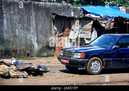 Vista esterna di una vecchia vettura Mercedes blu parcheggiata di fronte a fienili in ferro ondulato a Conakry, Guinea, Africa occidentale Foto Stock