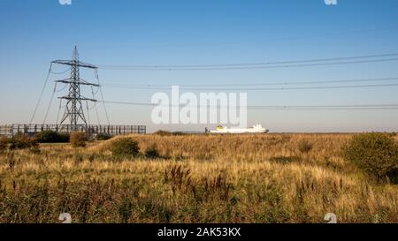 Gravesend, England, Regno Unito - 21 Settembre 2010: una nave cargo vele sull'estuario del Tamigi accanto a terra desolata e linee di alimentazione a Gravesend. Foto Stock