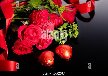 Rose rosse bouquet e a forma di cuore i cioccolatini, nastro rosso su sfondo nero Foto Stock