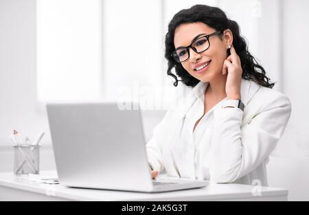 Il lavoro di ufficio concetto. Sorridente imprenditrice messicano lavorando sul computer portatile in ufficio moderno. Spazio di copia Foto Stock