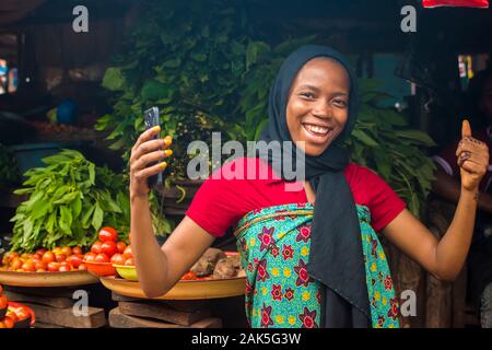 Donna africana la vendita di alimenti in un vivace mercato locale sensazione eccitato e felice di esprimere sollevando entrambe le mani facendo un pollice in alto, anche azienda ha Foto Stock