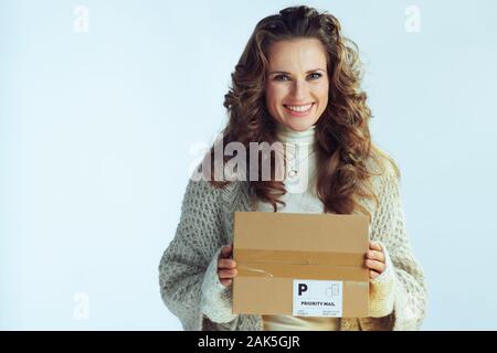 Ritratto di giovane felice casalinga con lunghi capelli ondulati in maglione collo e cardigan con pacco sulla luce invernale sfondo blu. Foto Stock