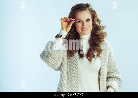 Felice donna elegante con lunghi capelli ondulati in maglione collo e cardigan spiumatura sopracciglia sulla luce invernale sfondo blu. Foto Stock