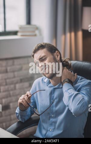 Sensazione di cattivo. Giovane uomo barbuto in maglietta blu che soffrono di dolore al collo Foto Stock