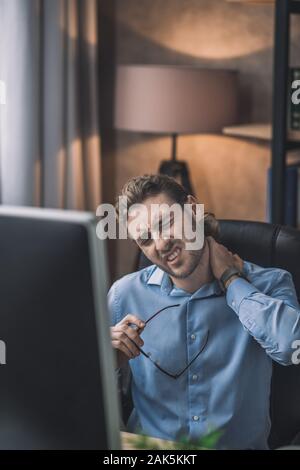 Dolore al collo. Giovane uomo barbuto in maglietta blu sentire dolore nel suo collo Foto Stock