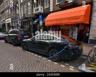 Amsterdam, Paesi Bassi, Agosto 2019. Un auto elettrica dal produttore Tesla. Essa è stata parcheggiata in corrispondenza di una stazione di carica. Il cavo blu è collegato Foto Stock