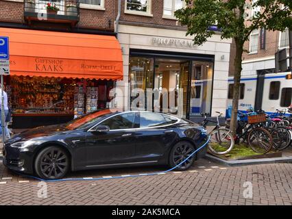 Amsterdam, Paesi Bassi, Agosto 2019. Un auto elettrica dal produttore Tesla. Essa è stata parcheggiata in corrispondenza di una stazione di carica. Il cavo blu è collegato Foto Stock