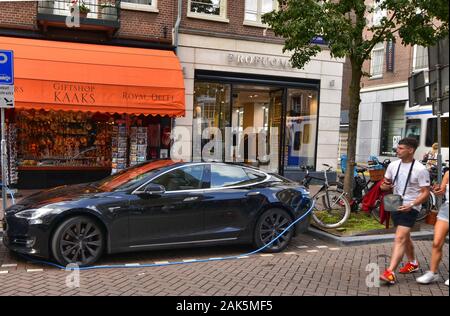Amsterdam, Paesi Bassi, Agosto 2019. Un auto elettrica dal produttore Tesla. Essa è stata parcheggiata in corrispondenza di una stazione di carica. Il cavo blu è collegato Foto Stock