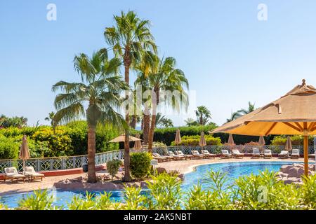 Sharm El Sheikh, Egitto - 11.04.2019: Hyatt Regency Sharm El Sheikh Resort. Piscina e lettini con ombrelloni circondati da una lussureggiante vegetazione tropicale. Foto Stock