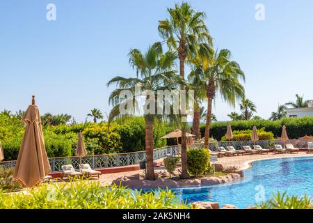 Sharm El Sheikh, Egitto - 11.04.2019: Hyatt Regency Sharm El Sheikh Resort. Piscina e lettini con ombrelloni circondati da una lussureggiante vegetazione tropicale. Foto Stock