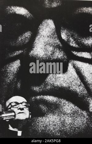 Fine 1970s fotografia vintage in bianco e nero di un diffusore con la sua immagine proiettata sul muro dietro di lui. Foto Stock