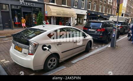 Amsterdam, Olanda. Agosto 2019. Sulla strada di una Toyota prius plug in è parcheggiato in ricarica. Il connettore di carica è stata inserita nell'appropria Foto Stock