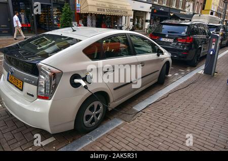 Amsterdam, Olanda. Agosto 2019. Sulla strada di una Toyota prius plug in è parcheggiato in ricarica. Il connettore di carica è stata inserita nell'appropria Foto Stock