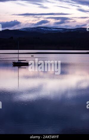 Barca a vela sul Loch Insh al crepuscolo con montagne innevate sullo sfondo, fotografato in Cairngorns National Park, Scozia Foto Stock