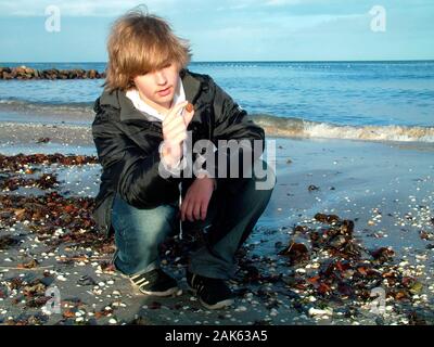 Il ragazzo osserva una pietra d'ambra sulla spiaggia Foto Stock