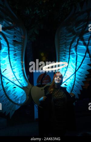 Femmina si trovava accanto alle ali illuminate dell'angelo e guardava un alone alla Leeds Light Night, Leeds, West Yorkshire, Inghilterra, UK. Foto Stock