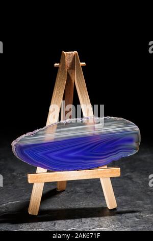 Studio shot di una forma allungata e sottile e lucido fetta di agata nella luce anteriore con strisce blu e bianche in piedi orizzontalmente su un cavalletto in miniatura. Foto Stock