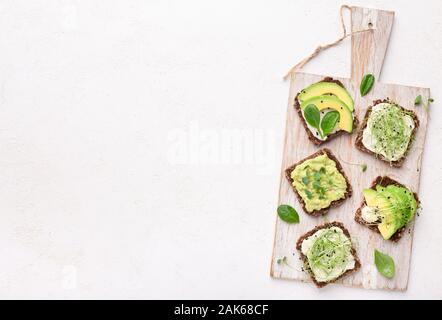 Sana panini integrali con avocado, tofu e microgreens sul tagliere, vista dall'alto, spazio vuoto Foto Stock