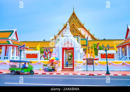 BANGKOK, Tailandia - 15 Aprile 2019: Il tuk-tuk rickshaw sorge presso le porte aperte di Wat Suthat tempio con una vista sul cortile interno del famoso re Foto Stock