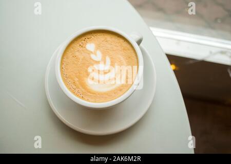 Tazza di cappuccino con belle latte art su una tavola di legno in un cafe con copyspace. Foto Stock