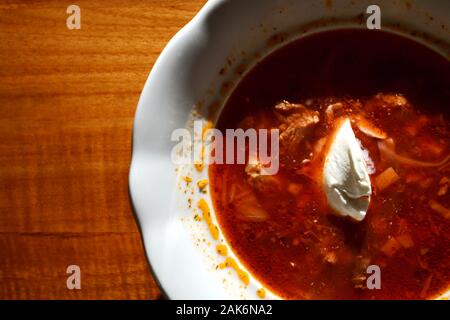 Scorpacciata di borscht calda zuppa di barbabietole, manzo, maiale, cavolo e carote, panna acida sulla parte superiore, tavolo in legno sfondo Foto Stock