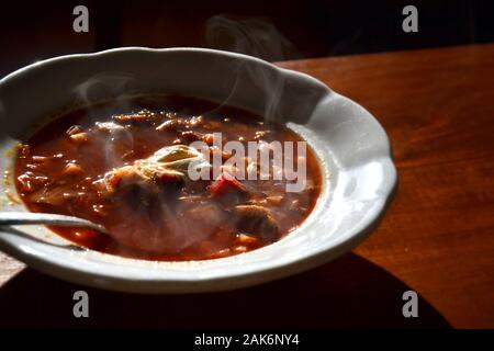 Scorpacciata di borscht calda zuppa di barbabietole, manzo, maiale, cavolo e carote, panna acida sulla parte superiore, tavolo in legno sfondo Foto Stock