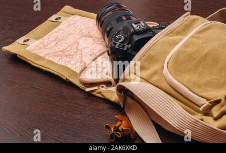 La fotocamera è in una borsa da viaggio che si estende su una superficie di legno Foto Stock