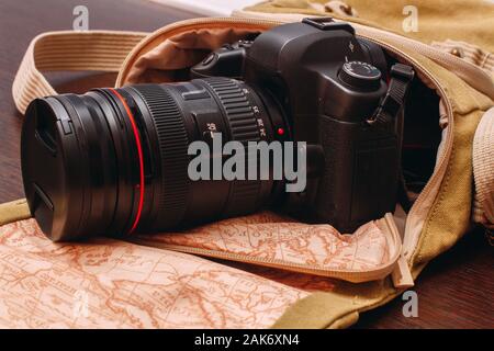 La fotocamera è in una borsa da viaggio che si estende su una superficie di legno Foto Stock