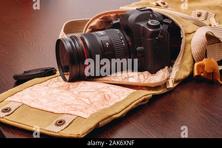 La fotocamera è in una borsa da viaggio che si estende su una superficie di legno Foto Stock