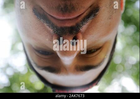 Ampio angolo ritratto di un uomo. Close-up del naso e mustaches, presa dal basso. Alberi verdi e luminose sullo sfondo. Foto Stock