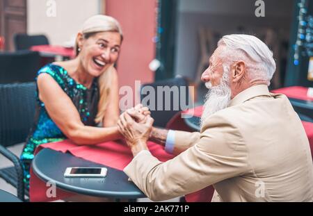 Felice coppia senior tenendo le mani mentre è seduto in un bar all'aperto - Elegante coppia marito e moglie cerca ogni altra mentre vi rilassate in un ristorante Foto Stock