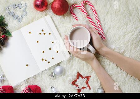 Vista dall'alto di mani tenendo calda tazza di caffè nei pressi di carta nota per il nuovo anno gli obiettivi e Elenco risoluzioni Foto Stock