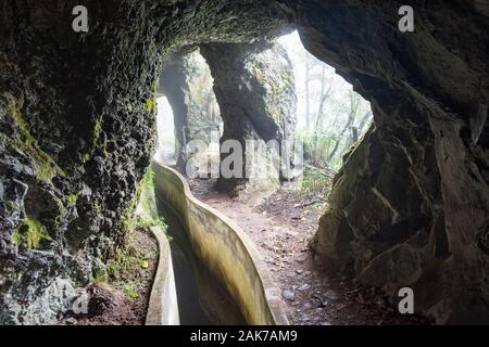 La Levada fare Furado sull' isola di Madeira, Portogallo inizia a muoversi intorno alla montagna attraverso un tunnel nella roccia con la luce del sole che esplodevano in varchi di attraversamento. Foto Stock