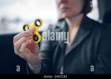 Imprenditrice giocando con agitano: spinner in auto mentre seduta sul sedile posteriore del veicolo e il pendolarismo per lavoro, il fuoco selettivo Foto Stock