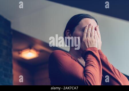 Premuto donna che ricopre la faccia con le mani e a piangere in appartamento loft, il fuoco selettivo Foto Stock